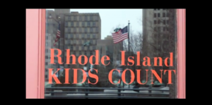 Logo on the window for the Rhode Island Kids Count office with a reflection of the American flag in the background.