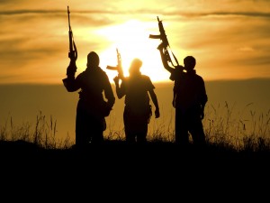 Photograph of soldiers with guns raised to the sky in a field of grass silhouetted against a yellow sunset.