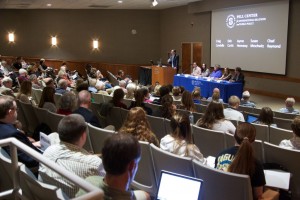 Pell Center Executive Director Jim Ludes moderates the lecture about Pope Francis' encyclical letter as panelists Craig Condella, Deb Curtis, Jayme Hennessy, Susan Meschwitz and Chad Raymond look out upon a crowd of Salve students and Newport community members