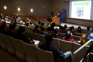 Dr. William Issel speaks at the podium during his lecture about racial justice in the 1960s as students and community members look on.