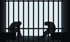 Image of the silhouettes of two prisoners hunched over inside a jail cell.