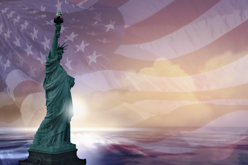 Image of the Statue of Liberty at sunset superimposed over a waving American flag.