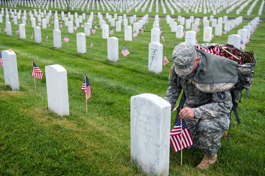 Soldier placing American flag at the base of each stone in Arlington National Cemetery.