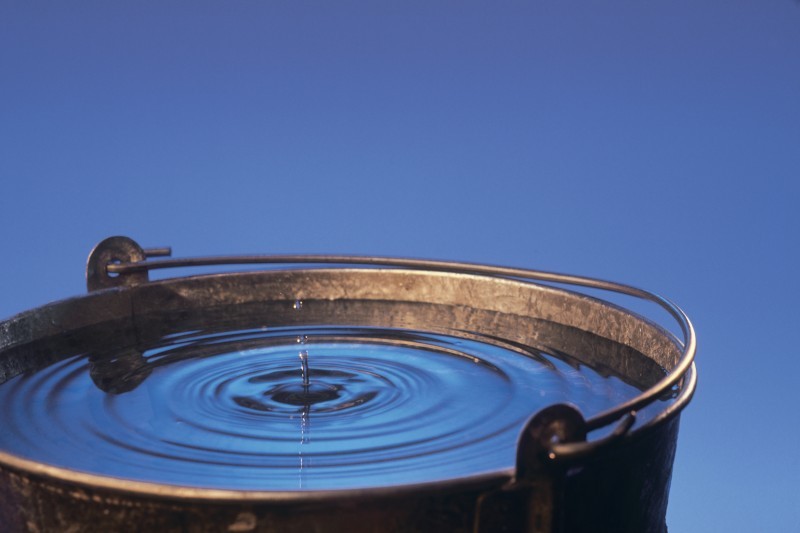 Close-up photo of a water droplet impacting the surface of a water bucket.