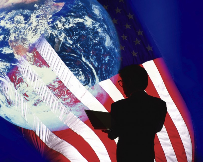 Image of a Businessman Holding a Laptop, Surrounded By an American Flag and the Planet Earth