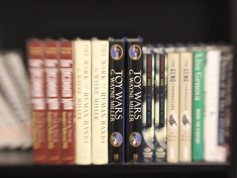 Books on a bookshelf, blurred background and sharp focus on the title "Toy Wars" by G. Wayne Miller.