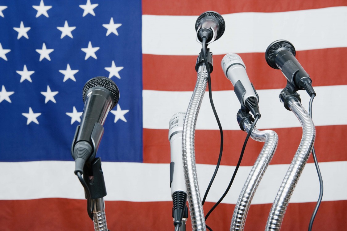 A series of microphones sitting in front of an American flag